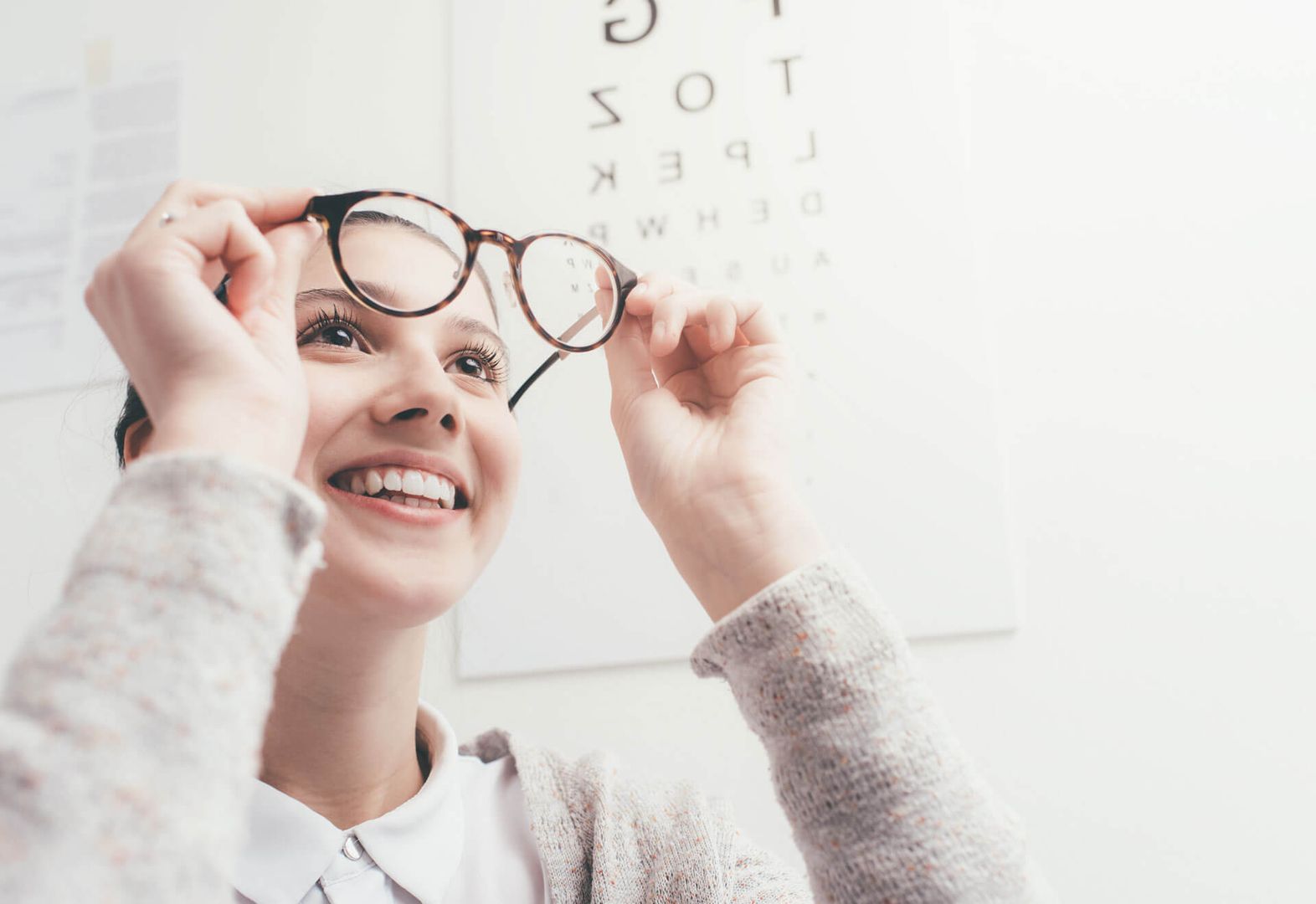 Ein Mädchen lächelt, während sie ihre Brille hochhält.